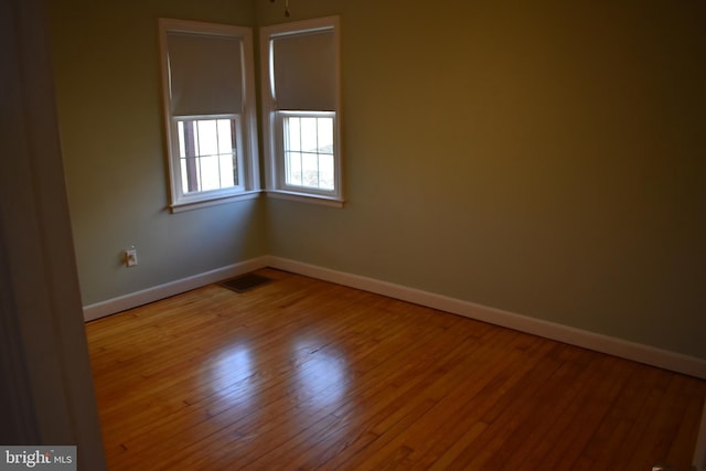 spare room with visible vents, baseboards, and hardwood / wood-style flooring