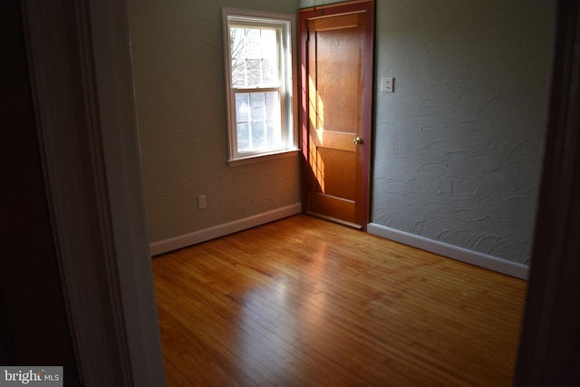 unfurnished room with light wood-style flooring, baseboards, and a textured wall