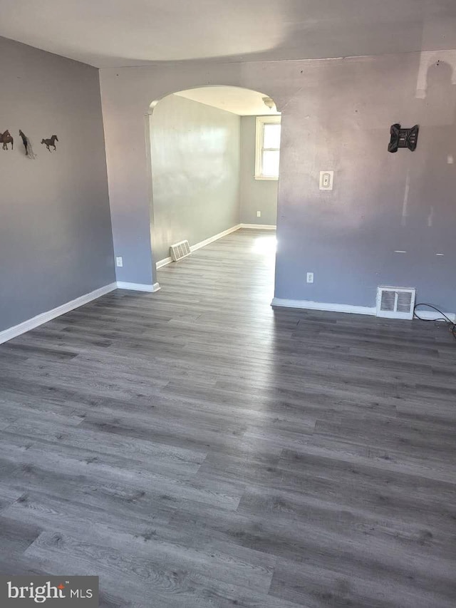 empty room with arched walkways, visible vents, baseboards, and wood finished floors