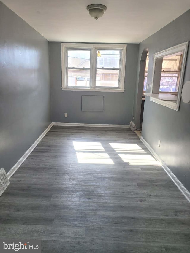 unfurnished room featuring visible vents, baseboards, arched walkways, and wood finished floors