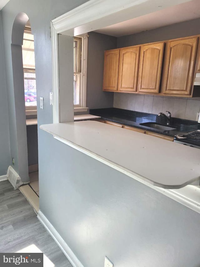 kitchen featuring visible vents, baseboards, light wood-style floors, arched walkways, and a sink