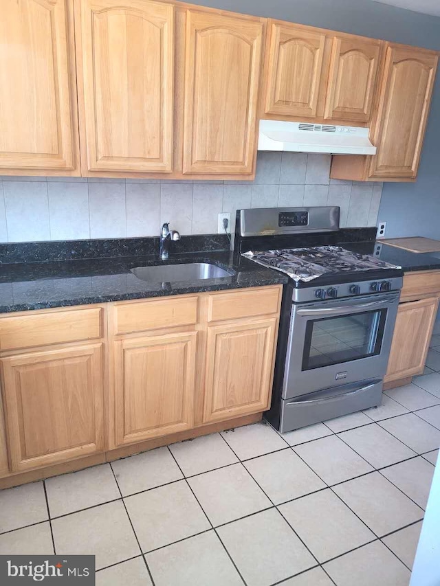 kitchen with light brown cabinets, under cabinet range hood, dark stone countertops, gas stove, and a sink