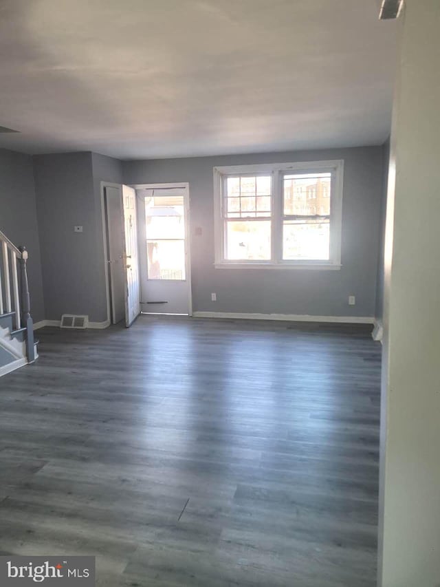 unfurnished living room with visible vents, baseboards, dark wood-type flooring, and stairway