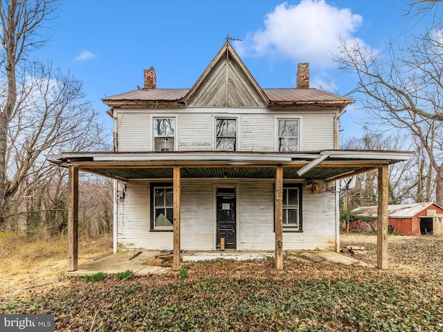 view of front facade featuring metal roof, brick siding, covered porch, and a chimney