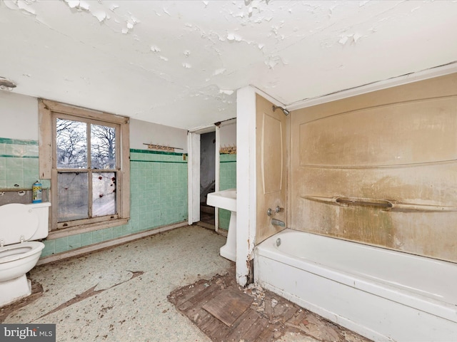 bathroom featuring a wainscoted wall, tile walls, toilet, and a tub