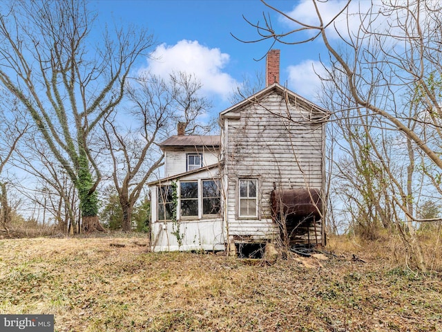 back of house with heating fuel, a sunroom, and a chimney