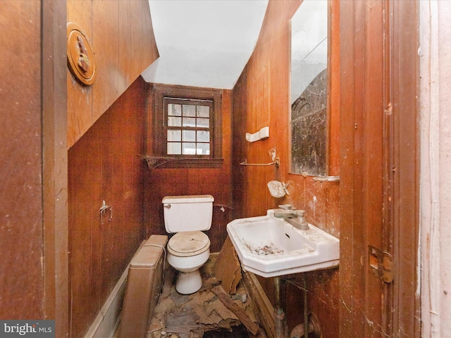 half bathroom with wooden walls, toilet, and a sink