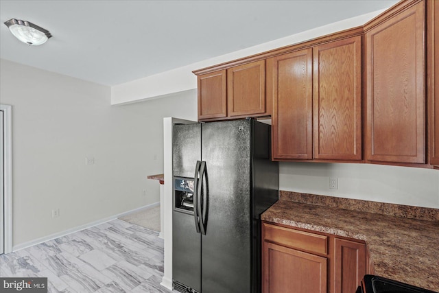 kitchen with brown cabinets, range with electric cooktop, dark countertops, baseboards, and black refrigerator with ice dispenser