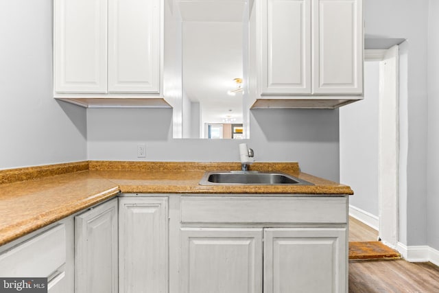 kitchen featuring white cabinets, wood finished floors, baseboards, and a sink