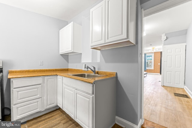 kitchen featuring a sink, visible vents, baseboards, white cabinetry, and wood finished floors
