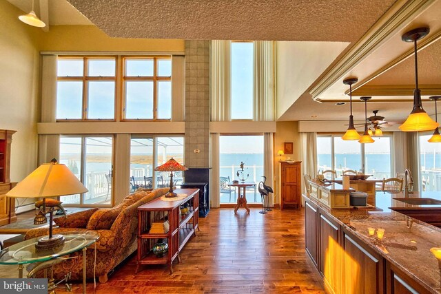 living area with a towering ceiling, a baseboard heating unit, ceiling fan, and dark wood-style flooring