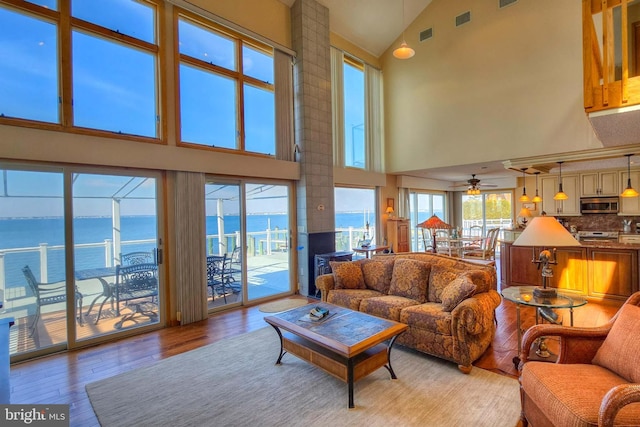 living area with visible vents, a water view, light wood-style flooring, high vaulted ceiling, and a ceiling fan