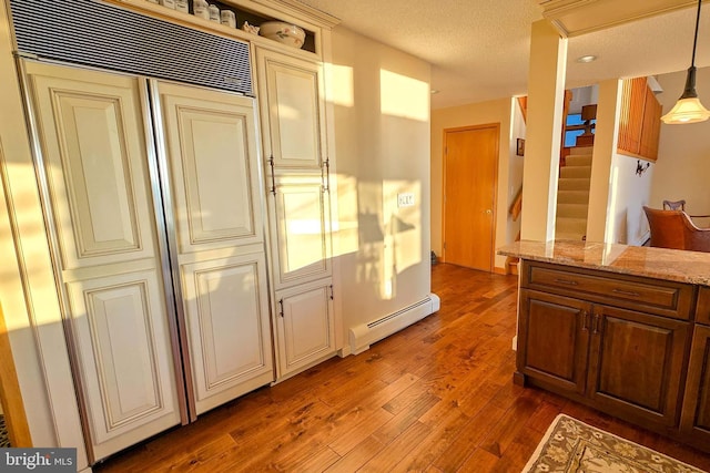 kitchen with light stone counters, a baseboard heating unit, cream cabinets, a textured ceiling, and wood finished floors