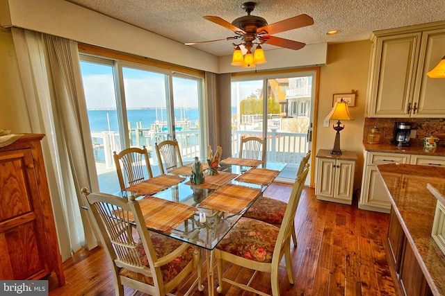 dining room featuring dark wood-style floors, a textured ceiling, a ceiling fan, and a water view