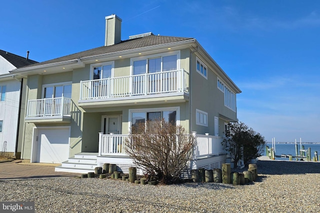 back of property featuring stucco siding, driveway, a garage, a balcony, and a chimney