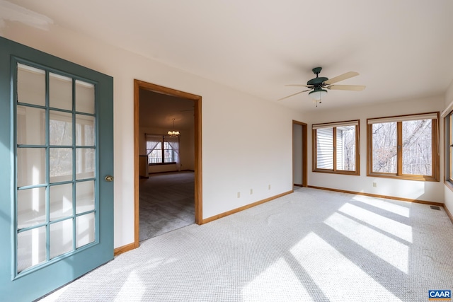 carpeted spare room with a wealth of natural light, visible vents, ceiling fan with notable chandelier, and baseboards