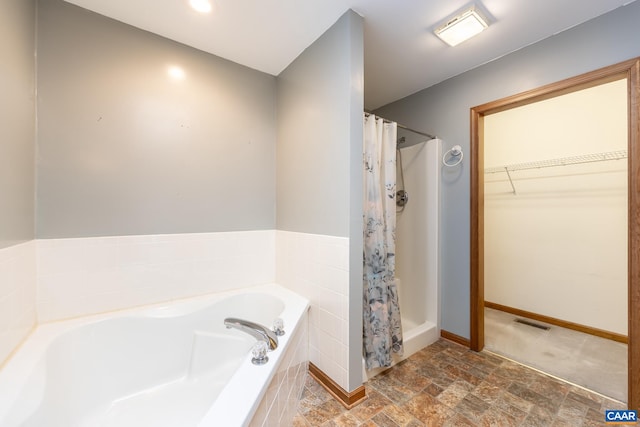 full bath featuring a spacious closet, visible vents, baseboards, a bath, and stone finish floor