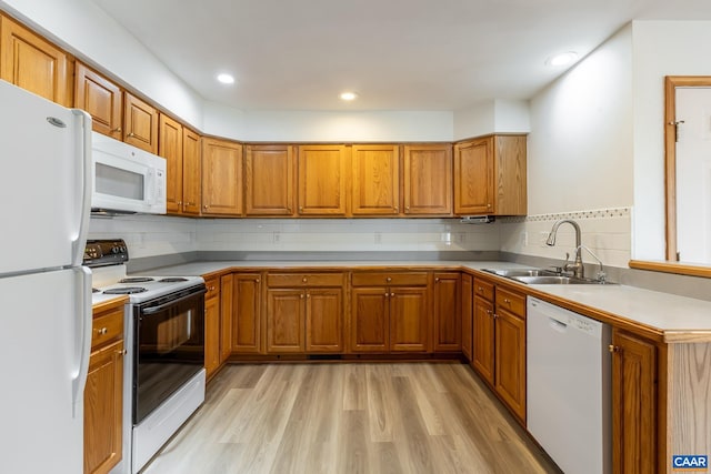 kitchen with backsplash, light wood-style flooring, brown cabinetry, white appliances, and a sink