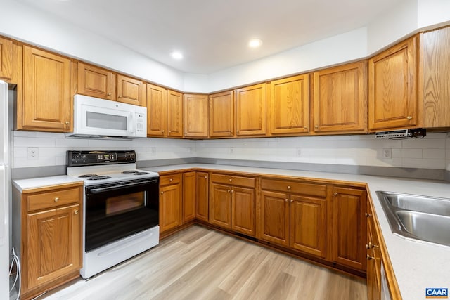 kitchen featuring brown cabinetry, white microwave, light wood finished floors, a sink, and range with electric cooktop