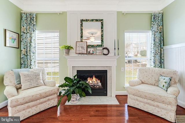 living area featuring plenty of natural light, wood finished floors, a high end fireplace, and ornamental molding