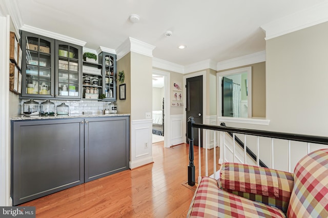 bar with ornamental molding, backsplash, wainscoting, light wood finished floors, and indoor wet bar