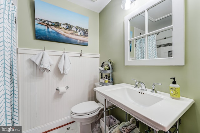 bathroom with curtained shower, toilet, and wainscoting