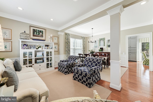 living area with a wainscoted wall, hardwood / wood-style floors, an inviting chandelier, crown molding, and decorative columns