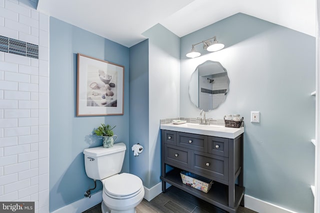 bathroom with vanity, wood finished floors, baseboards, walk in shower, and toilet