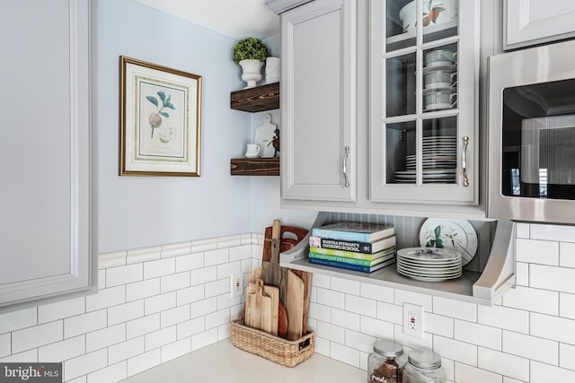 kitchen featuring stainless steel microwave, light countertops, tile walls, and open shelves