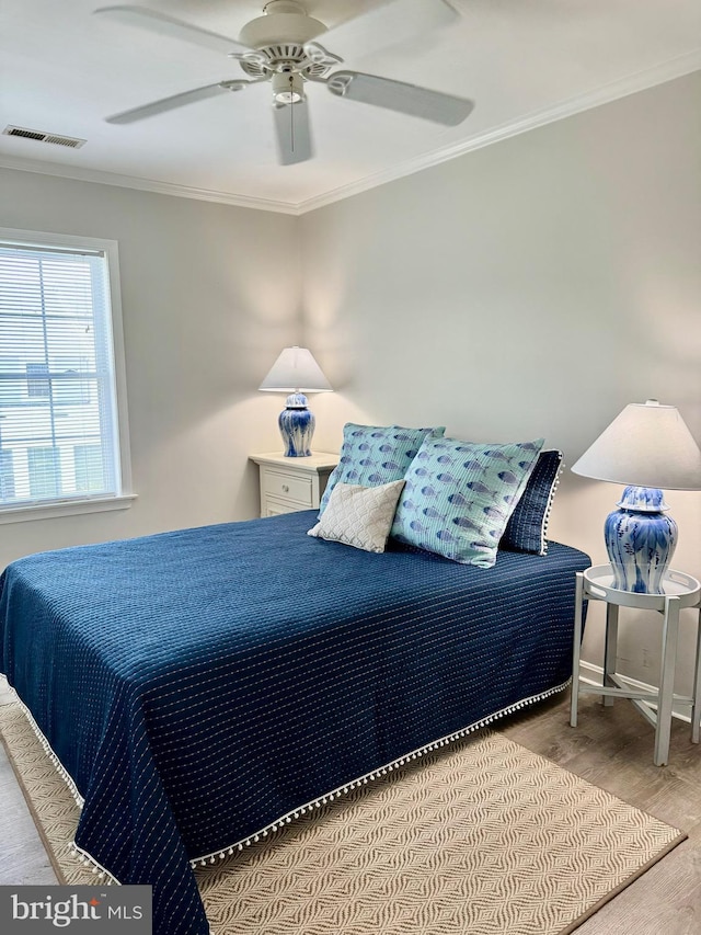 bedroom with crown molding, wood finished floors, visible vents, and baseboards