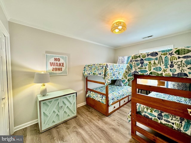 bedroom with baseboards, wood finished floors, visible vents, and ornamental molding