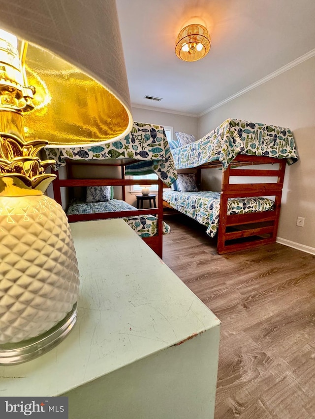 bedroom featuring visible vents, wood finished floors, baseboards, and ornamental molding