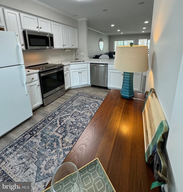 kitchen with light countertops, appliances with stainless steel finishes, wood finished floors, white cabinetry, and a sink