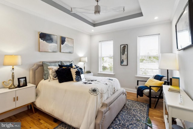 bedroom with ornamental molding, a tray ceiling, light wood-style floors, baseboards, and ceiling fan