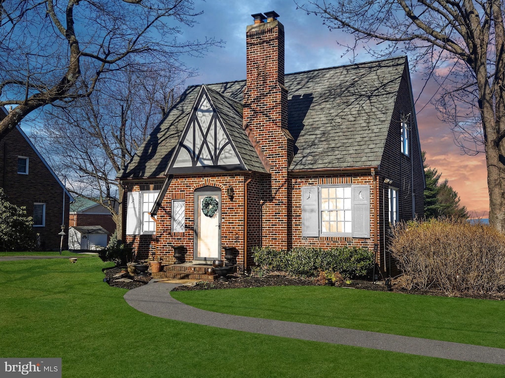 english style home with brick siding, a lawn, roof with shingles, and a chimney