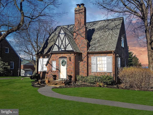 english style home with brick siding, a lawn, roof with shingles, and a chimney