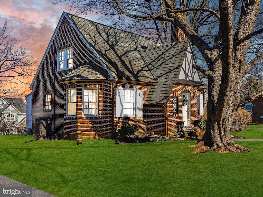 tudor house with brick siding, entry steps, a chimney, and a yard