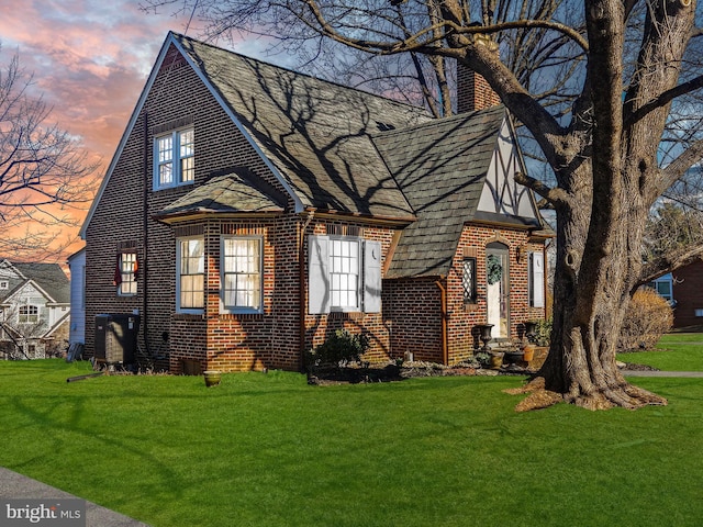 tudor house with brick siding, entry steps, a chimney, and a yard