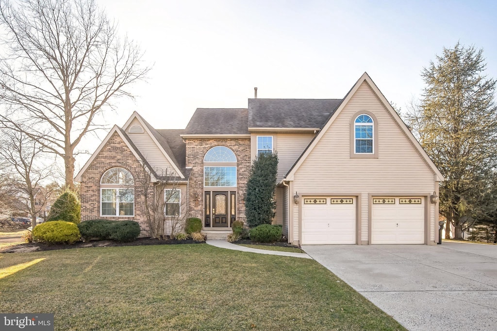 traditional-style home featuring a front lawn, concrete driveway, an attached garage, a shingled roof, and brick siding