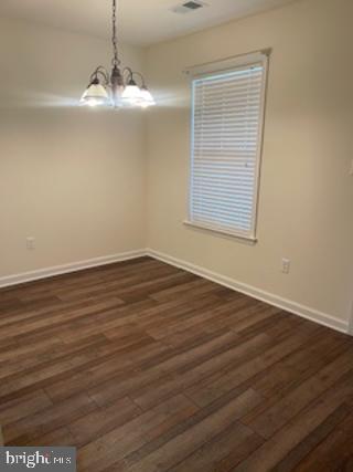 empty room with a chandelier, visible vents, dark wood-type flooring, and baseboards