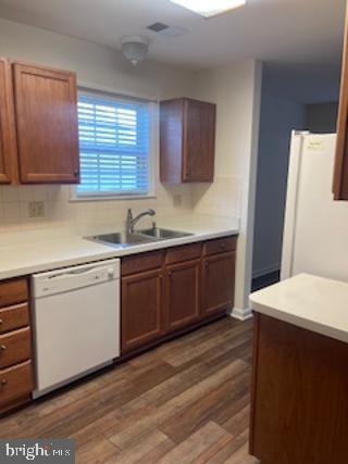 kitchen featuring a sink, wood finished floors, white appliances, light countertops, and decorative backsplash