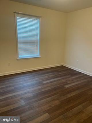 unfurnished room featuring baseboards and dark wood-style floors