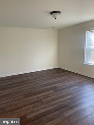 unfurnished room with baseboards and dark wood-type flooring