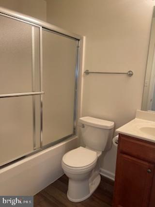 full bathroom with combined bath / shower with glass door, toilet, wood finished floors, and vanity