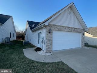 view of property exterior with a lawn, an attached garage, concrete driveway, and central AC