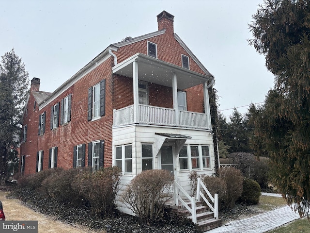 view of side of home with brick siding, a balcony, and a chimney