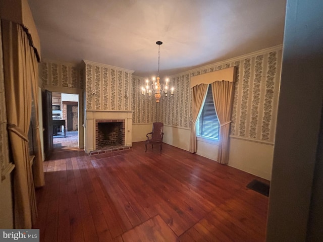 unfurnished living room with a notable chandelier, wallpapered walls, crown molding, and hardwood / wood-style flooring