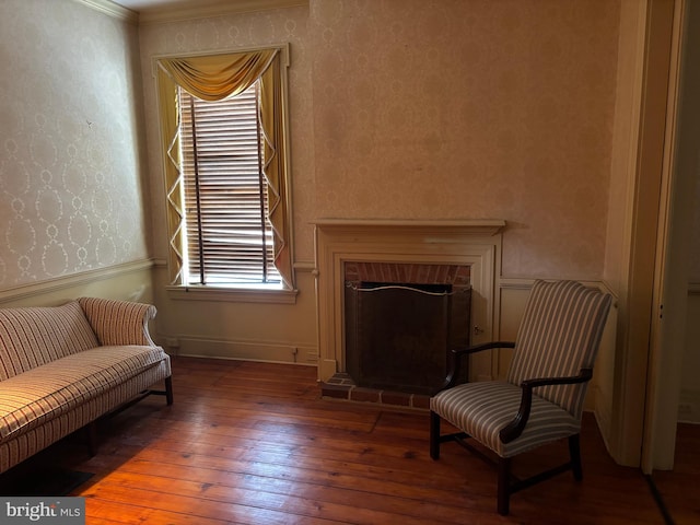 living area featuring wallpapered walls, hardwood / wood-style flooring, a brick fireplace, and baseboards