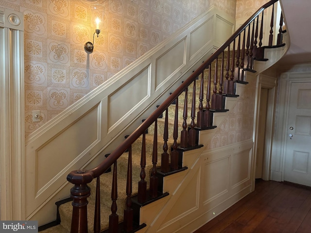 stairway featuring a decorative wall, wainscoting, wallpapered walls, and wood finished floors