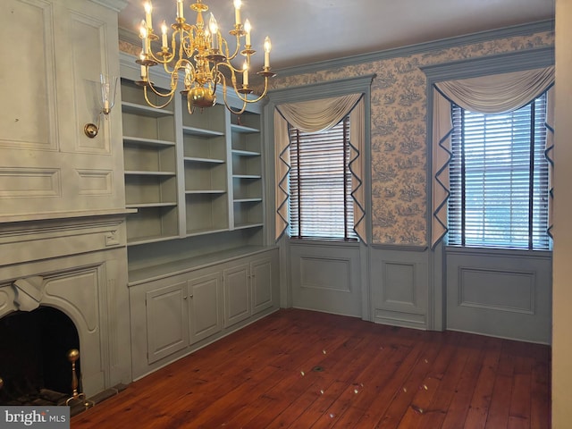 unfurnished dining area featuring wallpapered walls, a wainscoted wall, plenty of natural light, a notable chandelier, and dark wood-style flooring